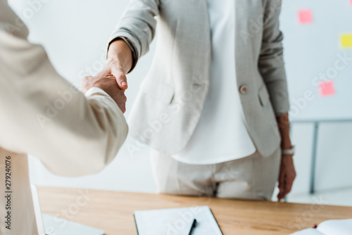 Fototapeta  cropped view of recruiter and employee shaking hands while standing in office