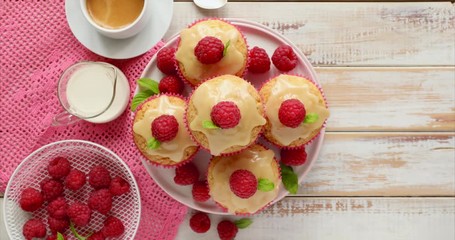 Wall Mural - Cupcakes with white chocolate and fresh raspberries on a on a rotating ceramic plate on a wooden white table, close up. A delicious dessert or breakfast.