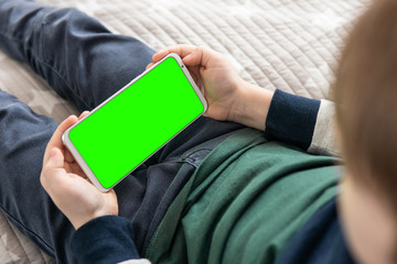 Wall Mural - Smartphone with a hromakey in the hands of a child. Phone a for keying is holding kid top view close up. Smartphone with a green screen in hand child .