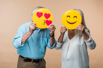 Wall Mural - senior couple covering faces with yellow smileys isolated on beige