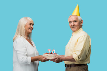 Wall Mural - cheerful retired man in party cap holding birthday cake near wife isolated on blue