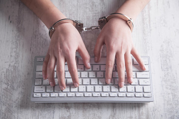 Hands in handcuffs typing on keyboard. Cyber Crime Concept