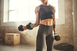 © Friends Stock - Perfect biceps. Young athletic woman with tattoo on her hand in sportswear exercising with dumbbells while standing in front of window at gym.