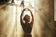 © Friends Stock - I love active life. Back view of young athletic woman in black sport clothing making heart shape with her hands while training in dark gym