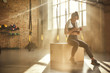 © Friends Stock - Staying in touch. Attractive athletic woman in headphones wearing towel on her shoulders and using smart phone while sitting at gym