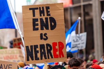 Homemade placard at ecological protest. An ecological campaigner is seen holding a sign saying the end is nearer during a march for the environment on a crowded city street.