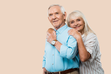 Wall Mural - cheerful retired woman hugging senior husband isolated on beige