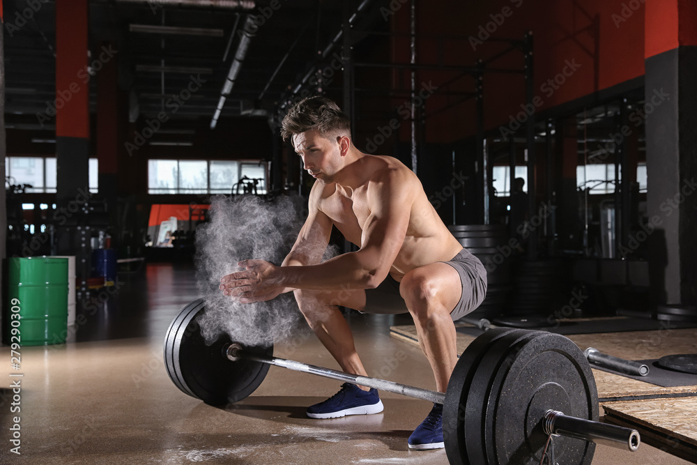 Sporty young man applying talc on hands before training with barbell in gym