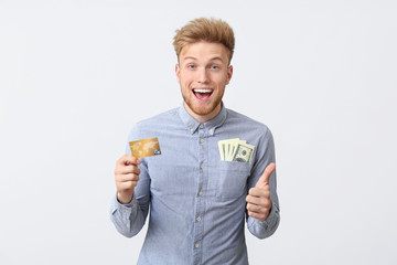 Canvas Print - Happy young man with credit card and dollars showing thumb-up gesture on white background