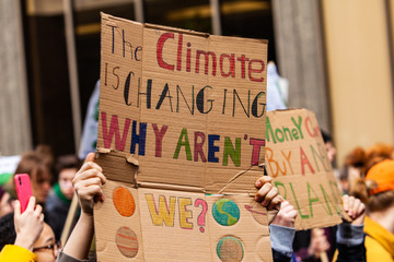 Homemade sign at environmental rally. A colorful cardboard placard is viewed close up, saying the climate is changing, why aren't we, in the hands of ecological activists as they protest in the city