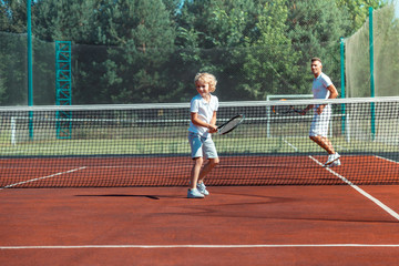 Wall Mural - Curly son laughing while playing tennis with daddy