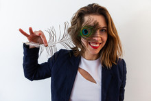 Fun Brown Haired Girl With Peacock Tail. A Playful Woman In Her Thirties Is Viewed From The Front, Happily Posing With A Peafowl Feather Held Over Her Eye, Smartly Dressed Accomplished Young Adult.