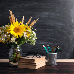 Glasses teacher books and wildflowers bouquet on the table, on background blackboard with chalk. The concept of the teacher's day. Copy space.