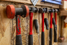 Selection Of Metalworking Mallets. A Closeup View On A Variety Of Metalwork Hammers And Mallets Inside A Workshop. Various Sizes And Styles Hanging On Screws For Easy Access.