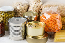 Various Canned Food And Raw Cereal Grains On A Table.