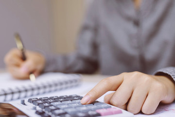 Close up young woman hand is writing in a notebook and using calculator counting making notes Accounting at doing finance at home office.  Savings finances concept. note pad