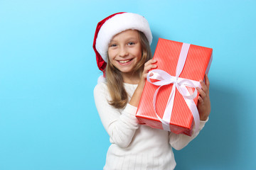 Wall Mural - cute cheerful girl in a Christmas hat on a colored background holding a gift