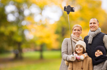 Wall Mural - family, childhood, season, technology and people concept - happy family taking selfie with smartphone and monopod in autumn park