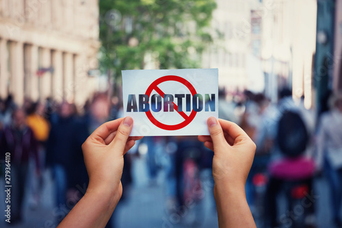 Activist hands holding a banner with stop abortion message over a crowded street background. Social awareness concept, humanity problems say no to abortion. Fetus rights law and reproductive justice