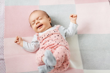 babyhood and people concept - sweet sleeping little baby girl in pink suit lying on knitted blanket