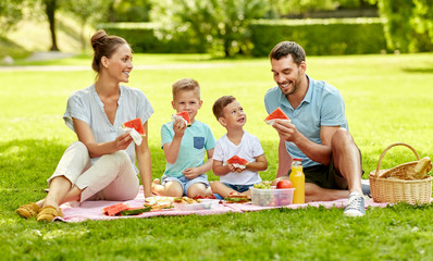 Wall Mural - family, leisure and people concept - happy mother, father and two little sons having picnic and eating watermelon at summer park