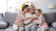 © motortion - Multi-generation females hugging on home sofa smiling camera, family closeness