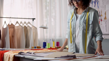 Concentrated on her work designer unfolding fabric on desk, personal atelier