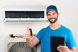 © stockphoto-graf - Installation service fix  repair maintenance of an air conditioner indoor unit, by cryogenist technican worker giving thumbs up ready to go after commissioning in blue shirt  baseball cap