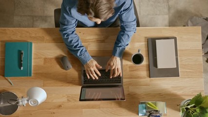 Wall Mural - Top View Zoom Out Shot: In the Office Businessman Sitting at the Wooden Desk Opens Laptop and Starts Working He Drinks Coffee, Types, Writes Emails, Surfs the Internet, Designs Software