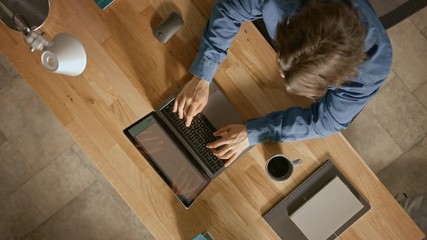 Poster - Top View Rotating Shot: Businessman Sitting at the Wooden Desk Works on a Laptop in his Home Office. He Drinks Coffee, Types, Writes, Surfs the Internet, Creates and Designs Software, Online Shopping