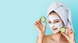 © Olesia - Beautiful young woman with facial mask on her face holding slices of cucumber. Skin care and treatment, spa, natural beauty and cosmetology concept.