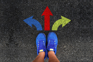 man legs in sneakers standing on road with three direction arrow choices, left, right or move forward