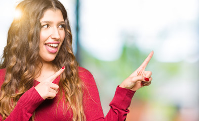 Young beautiful woman wearing red sweater smiling and looking at the camera pointing with two hands and fingers to the side.