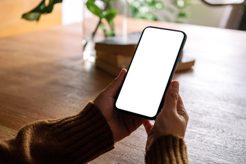mockup image of hands holding black mobile phone with blank desktop screen on wooden table