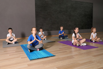 Wall Mural - Cute little children sitting on floor and doing physical exercise in school gym. Healthy lifestyle