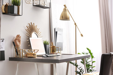 Modern workplace with laptop and golden decor on desk near wall. Stylish interior design