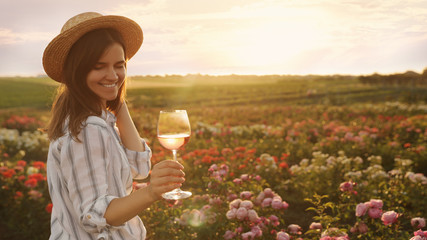 Canvas Print - Woman with glass of wine in rose garden on sunny day. Space for text