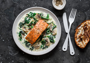 Wall Mural - Baked salmon with creamy spinach mushrooms sauce on a dark background, top view. Salmon florentine