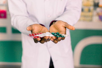 Wall Mural - Hands of African American man pharmacist holding tablets and pills, while standing in modern pharmacy