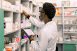 African American male pharmacist using digital tablet during inventory in pharmacy.