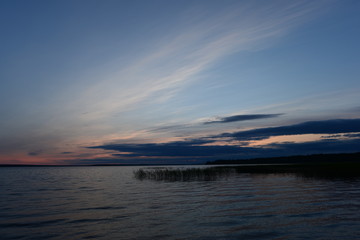 Wall Mural - Twilight blue sky in cirrus clouds at sunset in a dark blue cloud on the horizon above the water of the lake