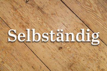 Wall Mural - `selbständig` white text on a wooden background. translation: `freelancer`