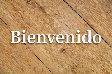 Wall Mural - `bienvenido` white text on a wooden background. translation: `welcome`