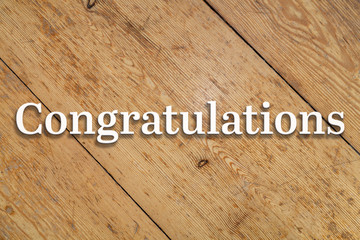 Wall Mural - 'congratulations' white text on a wooden background.