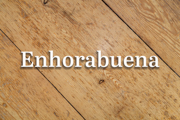 Wall Mural - 'enhorabuena' white text on a wooden background. translation: 'congratulations'