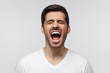 Angry man, rage concept. Close-up portrait of screaming with closed eyes crazy young man isolated, on gray background