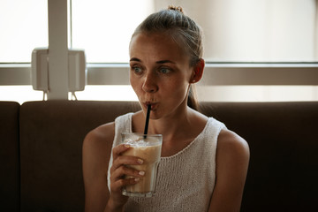 Beautiful cute girl drinking a coffee beverage through a straw sitting in the cafe near the window