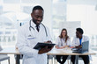 © gorynvd - Handsome Afro American doctor in white coat makes some notes. Young medical student with a stethoscope around his neck holds a folder.