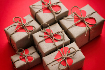 Set of brown gift boxes. Wrapped in craft paper and tied by hemp cord. Bright red background and carton hearts decorative card. 