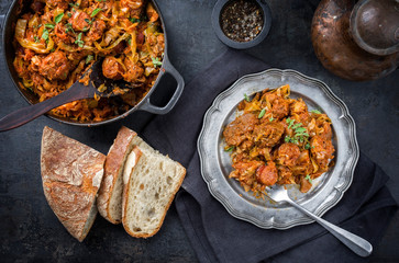 Traditional Polish kraut stew bigos with sausage, meat and mushrooms as top view in a cast iron pot and pewter plate on an old rustic board